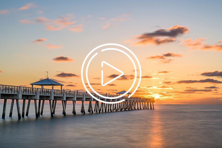 Juno Beach Pier during sunrise with play button overlay
